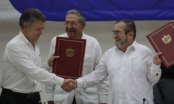 Colombian President Juan Manuel Santos, left, and Commander of the Revolutionary Armed Forces of Colombia or FARC, Timoleon Jimenez, right, shake hands during a signing ceremony of a cease-fire and rebel disarmament deal, in Havana, Cuba, Thursday, June 23, 2016.  The deal moves Colombia closer to ending a 52-year war that has left more than 220,000 people dead. Pictured in the center is Cuba's President Raul Castro. (AP Photo/Ramon Espinosa)