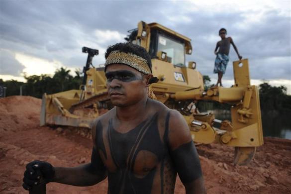 Two Amazon Indians stand near a heavy machinery being used in the construction of the massive Belo Monte hydroelectric dam, as they protest against the project in Vitoria do Xingu July 7, 2012. Some 300 natives have been occupying, since June 21, one of the main areas where construction work is being done on what potentially  will be the world's third largest hydroelectric dam, in protest against the project's environmental impact and the displacement of communities along the Xingu River. REUTERS/Lunae Parracho (BRAZIL - Tags: CIVIL UNREST ENVIRONMENT)